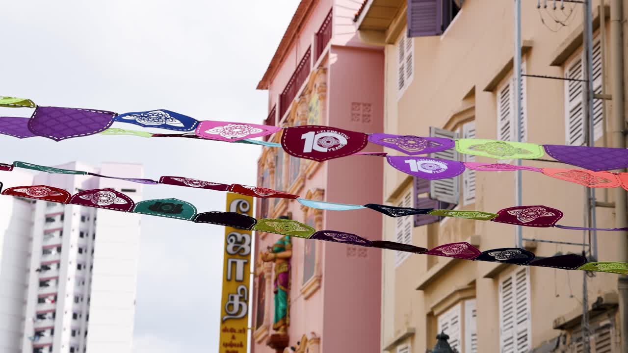 Decorações vibrantes de bandeirinhas de papel balançam ao vento sobre edifícios em tons pastel, luz do dia, rua urbana de Singapura