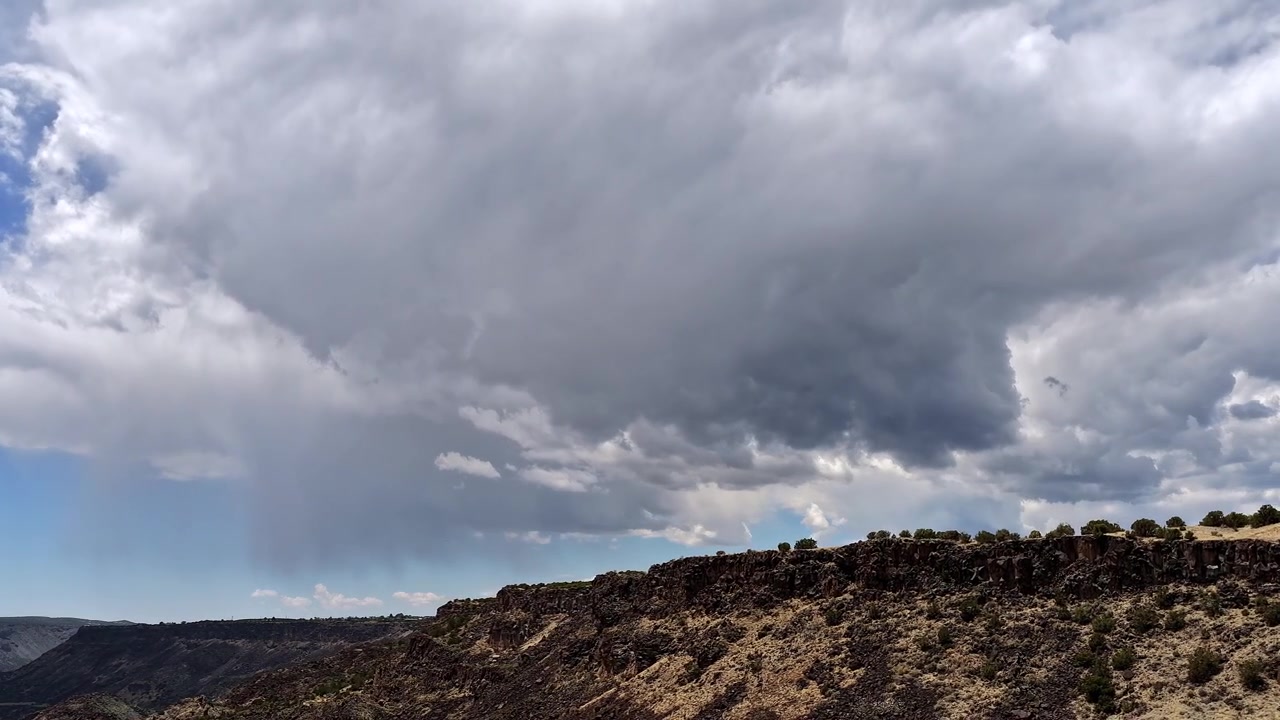 Un timelapse mozzafiato con drone che cattura una potente tempesta monsonica che si abbatte su una cresta rocciosa di un canyon nel sud-ovest. Nuvole scure e atmosferiche si addensano mentre scrosci di pioggia attraversano il maestoso altopiano desertico.