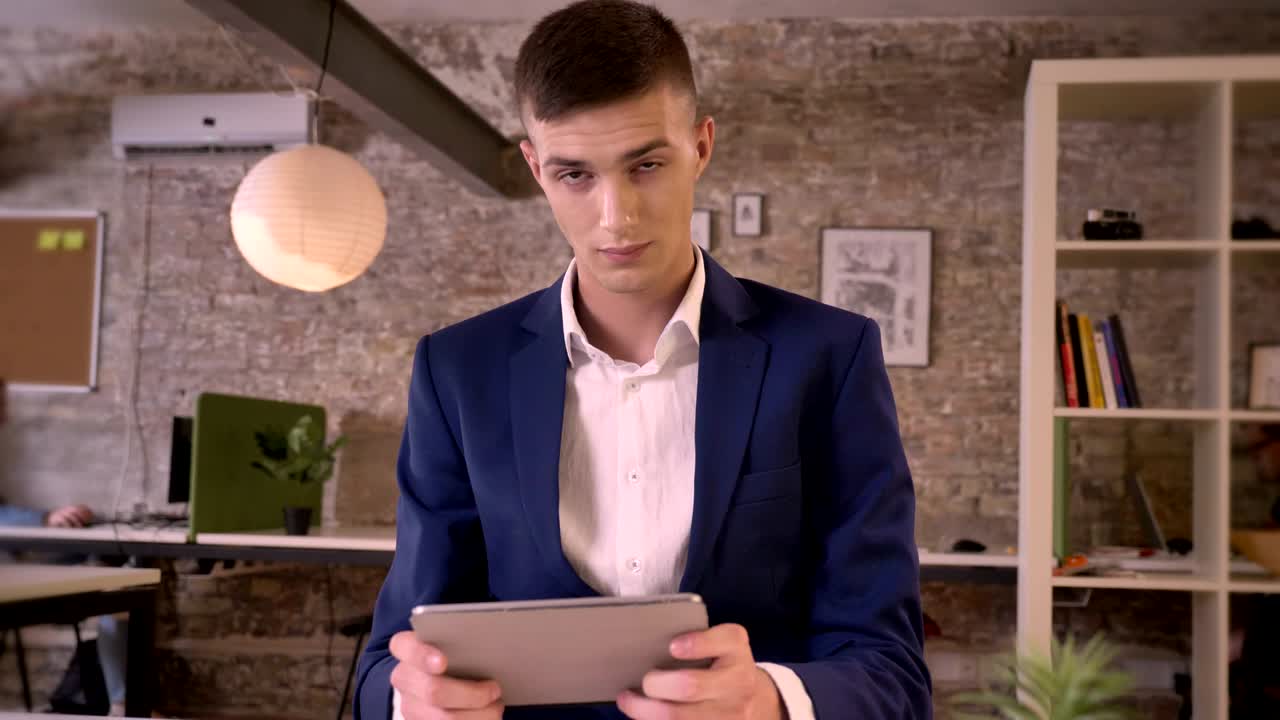Young concentrated businessman is watching in tablet, watching at camera, communication concept, business concept