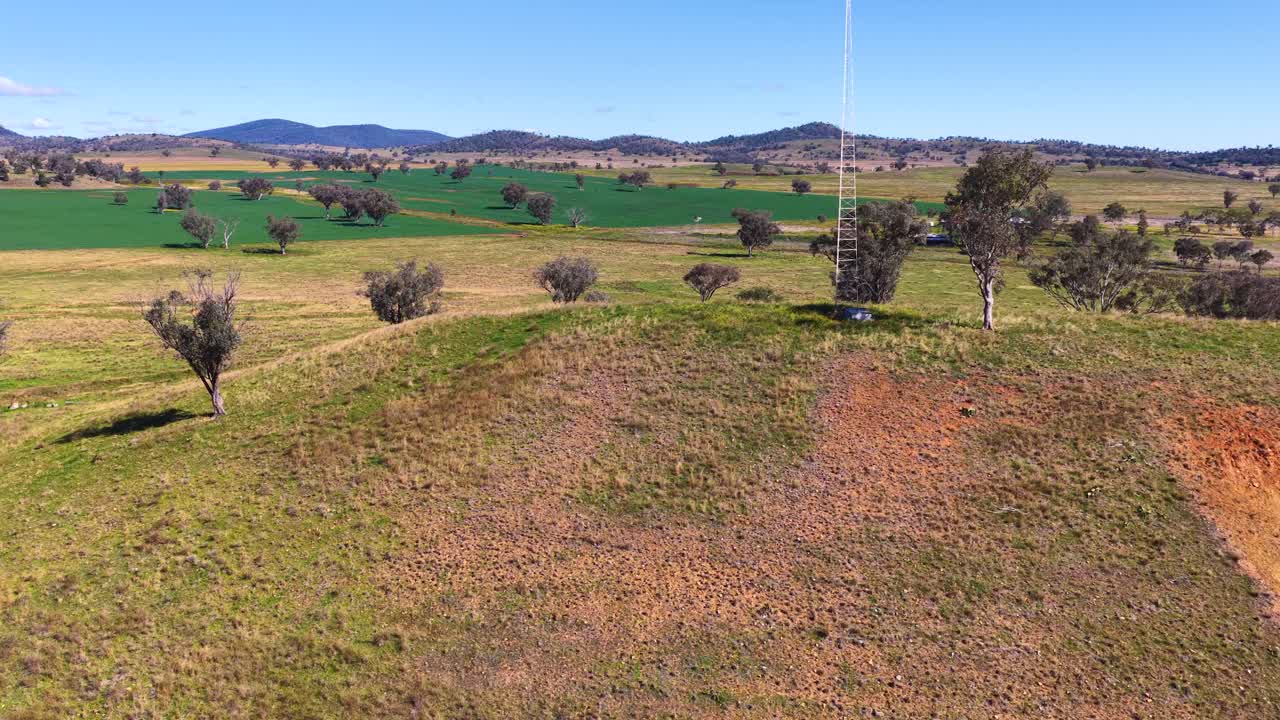 Drone flies above rural hill with trees and fields