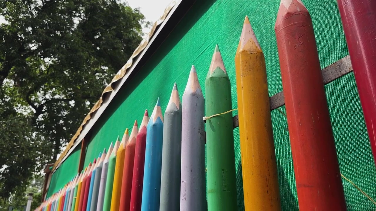Inquadratura ravvicinata di una decorazione a recinzione con matite colorate giganti installata lungo il muro di confine di una scuola, che rappresenta la creatività, l'educazione e uno spazio pubblico a misura di bambino
