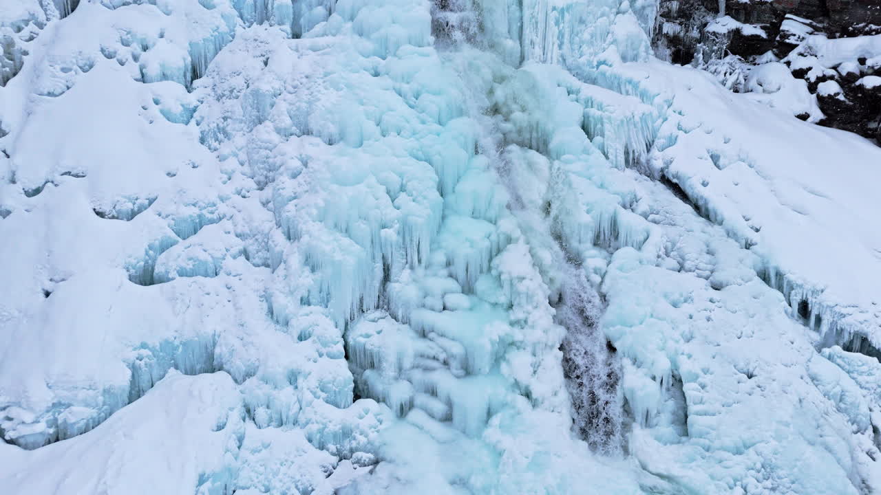 Frozen waterfall with icy blue formations and flowing water in Norway near Rovijoen Putous