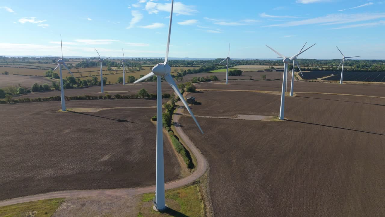 FPV drone view above rolling farmland and countryside with wind and solar energy systems, England, United Kingdom