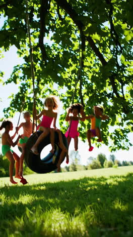 girls playing on a tire swing under a tree