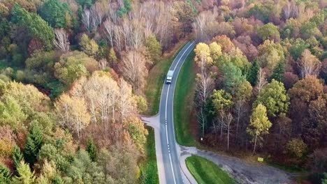 Toma-Aérea-De-Un-Camión-Que-Viaja-Por-Carretera-En-Un-Colorido-Bosque-Otoñal