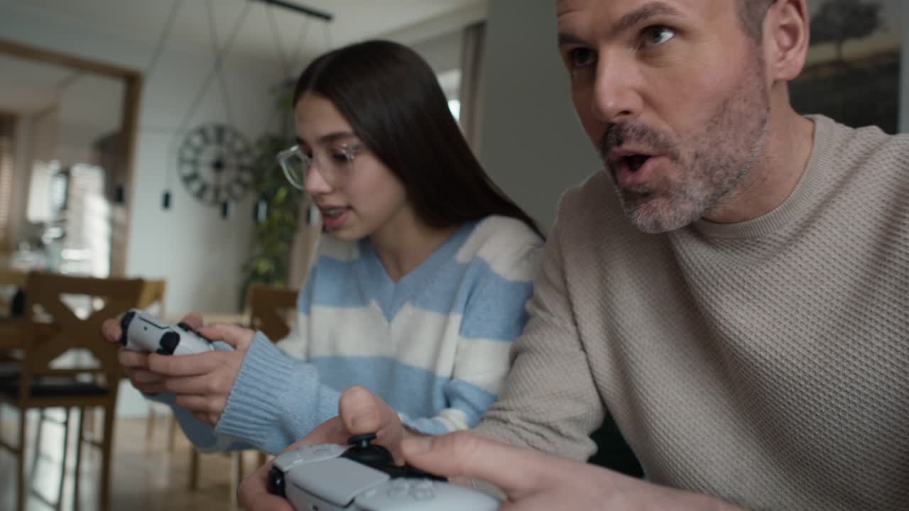adolescente caucásica y su padre jugando a un videojuego con un controlador de juego