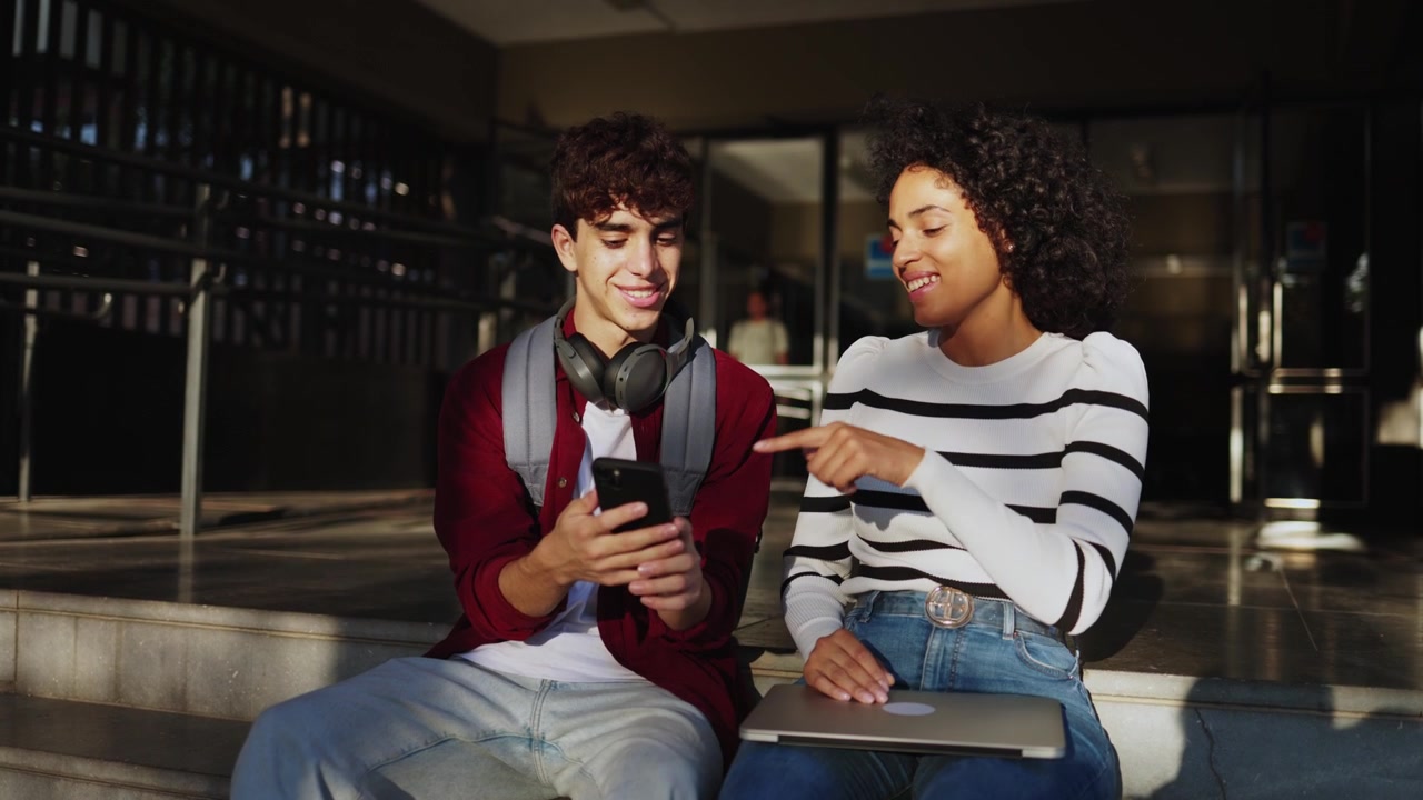 Two Students Sitting on Steps and Discussing Content on Smartphone