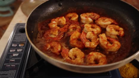Extreme-close-up-shot-capturing-professional-chef-swirling-the-shallow-frying-pan-on-the-portable-gas-stove,-evenly-distributed-the-peeled-prawns-with-delicious-sauce-of-red-paprika-spice