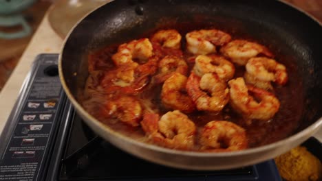 extreme close up shot capturing professional chef swirling the shallow frying pan on the portable gas stove, evenly distributed the peeled prawns with delicious sauce of red paprika spice