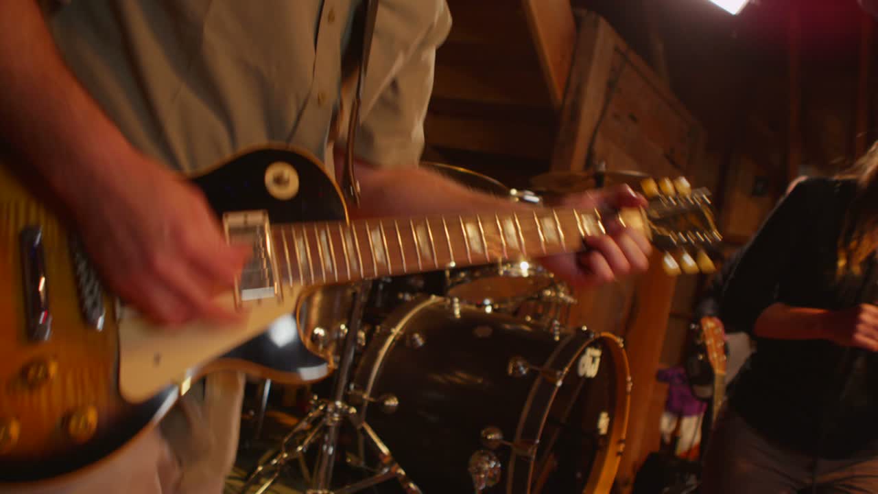 primer plano de un hombre tocando el bajo mientras una mujer con un micrófono baila en el fondo