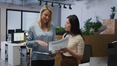 mujeres de negocios caucásicas y asiáticas discuten un informe en una oficina