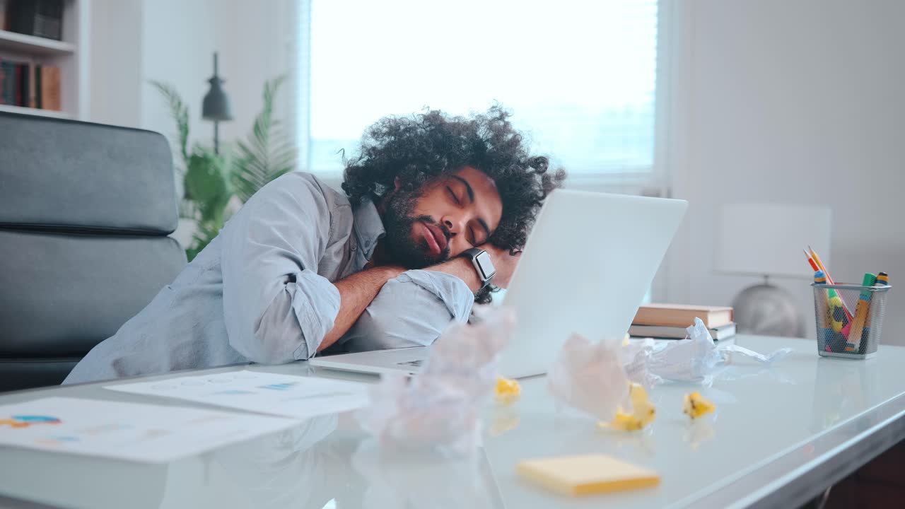 Young african american man freelancer sleeps with head on table next to laptop