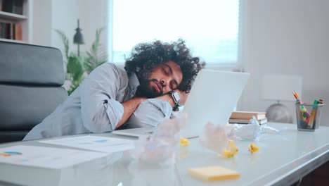 young african american man freelancer sleeps with head on table next to laptop