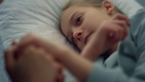 Cute-girl-lying-hospital-bed-portrait.-Mother-gently-holding-child-hand-closeup.