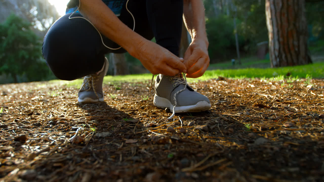 Donna anziana che si allaccia i lacci delle scarpe nel parco 4k