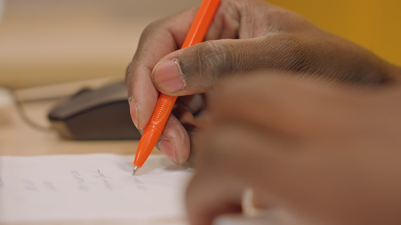 Studerende udfylder svar med kuglepen. Fokuseret studerende skriver svar på eksamensark under prøve. Koncentreret studerende færdiggør omhyggeligt eksamenssvar med orange kuglepen i et stille klasseværelse.