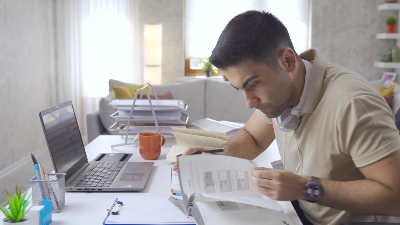Student looking at books and laptop at home.