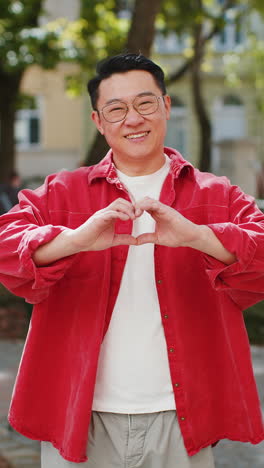 Asian-man-makes-symbol-of-love,-showing-heart-sign-to-camera,-express-romantic-positive-feelings