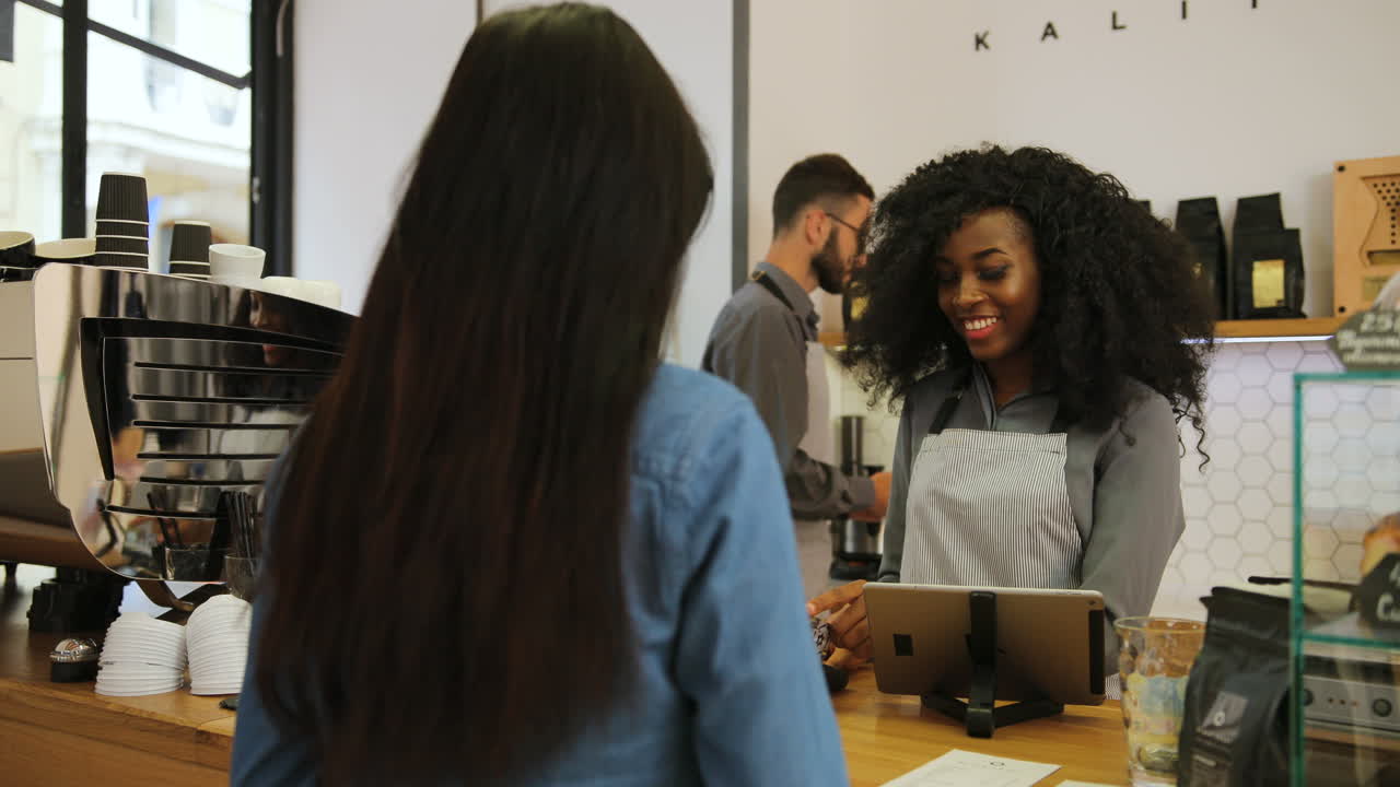 Rear view of a young caucasian woman paying for a coffe with credit card in a coffee shop