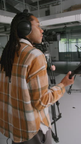 Vertical-Video-Of-Male-Sound-Recordist-And-Camera-Operator-Working-On-Film-Set-Shooting-Movie-Or-Video-In-Studio-Shot-In-Real-Time