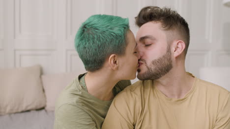 portrait of a happy couple kissing and talking while sitting on the bed at home