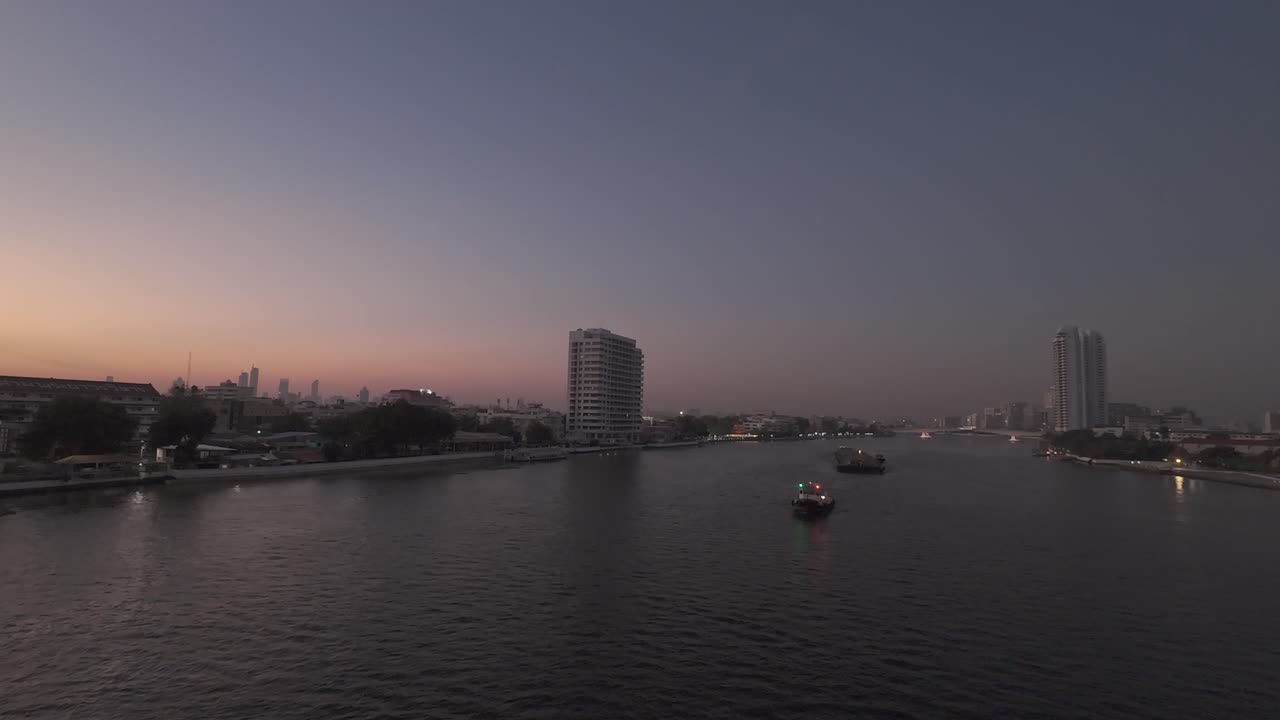 el crepúsculo desciende sobre un río tranquilo, reflejando las luces de la ciudad que se desvanecen mientras los barcos se desplazan a través de las aguas tranquilas.