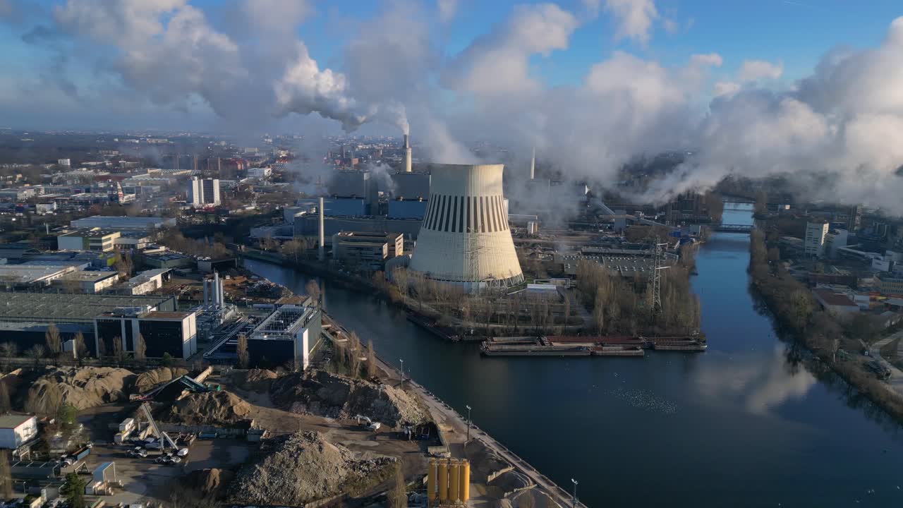 power plant emitting steam from its cooling tower, situated by a river and overlooking the cityscape. Great aerial view flight wide orbit overview drone