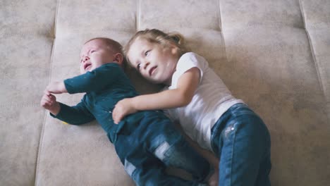 little girl in white tshirt hugs crying brother on large bed