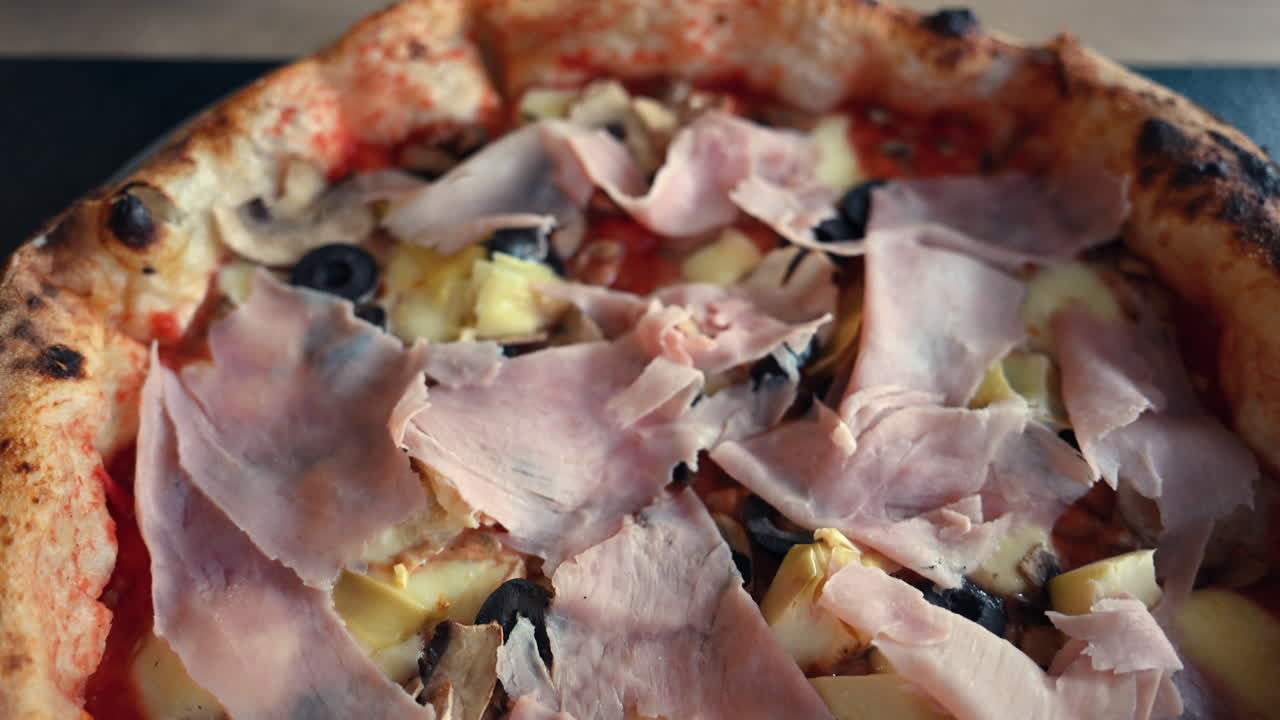 Primo piano di pizza appena sfornata condita con prosciutto, olive, funghi e formaggio