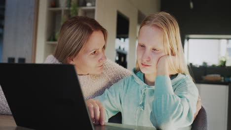 a woman sits next to a sad daughter next to a laptop. family communication and support