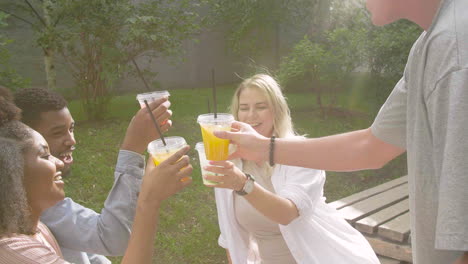 joven llevando una bandeja de bebidas refrescantes para llevar a sus amigos multiétnicos y brindando juntos en un parque