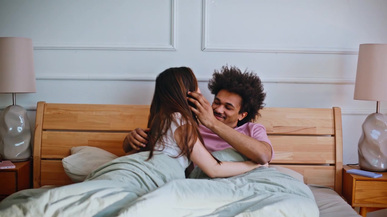 Man stretching arms bed embracing girlfriend. Happy interracial couple morning.
