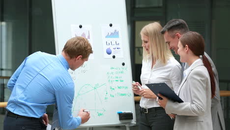 Gruppe-Von-Kollegen,-Die-über-Eine-Präsentation-Von-Finanzdiagrammen-Auf-Einem-Whiteboard-Sprechen