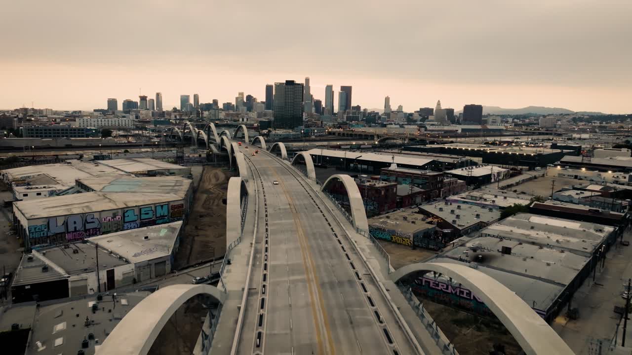 A slow moving low angle drone shot of the Ribbon Of Light 6th Street Bridge during sunset in Los Angeles California with cars driving in the foreground of the city's skyline