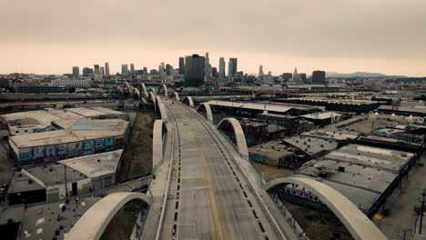 A-slow-moving-low-angle-drone-shot-of-the-Ribbon-Of-Light-6th-Street-Bridge-during-sunset-in-Los-Angeles-California-with-cars-driving-in-the-foreground-of-the-city's-skyline