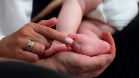hands of adults touching cute tiny newborn's feet. happy mom's finger caressing little baby toes. close up.