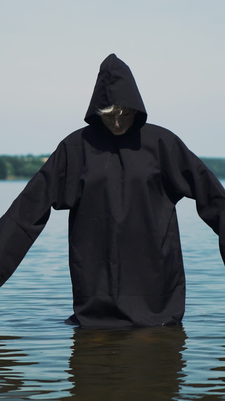 Scary figure in black mantle in the river. Halloween costume. Vertical video