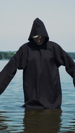 scary figure in black mantle in the river. halloween costume. vertical video