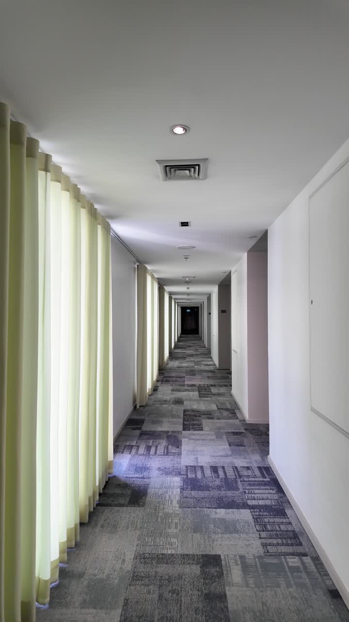 Bright, empty hotel corridor with pale curtains, soft lighting, and a patterned carpet, conveying calm and solitude