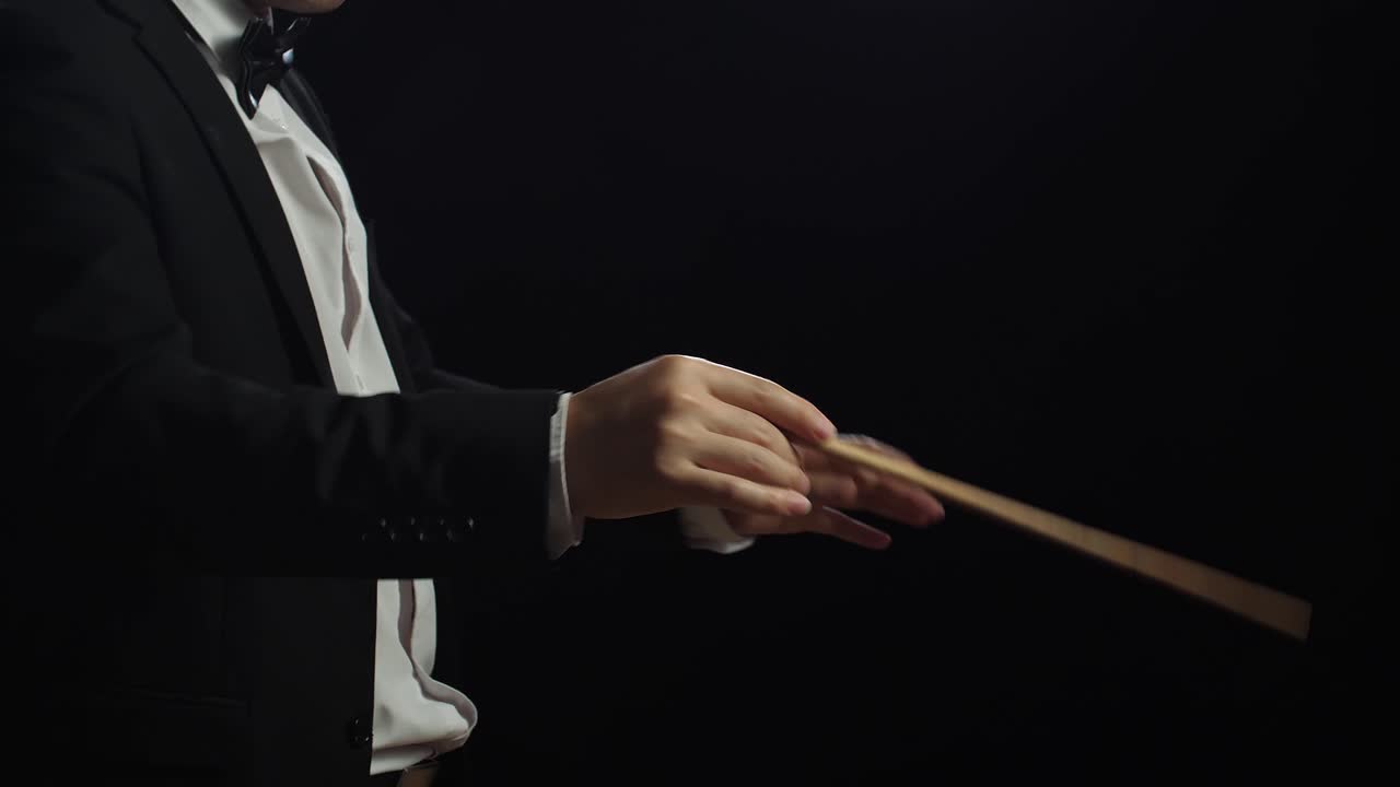 vista lateral cercana de las manos del director sosteniendo un bastón y moviéndose en el estudio negro