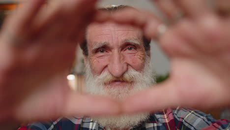 senior grandfather man makes symbol of love, showing heart sign to camera, express romantic feelings