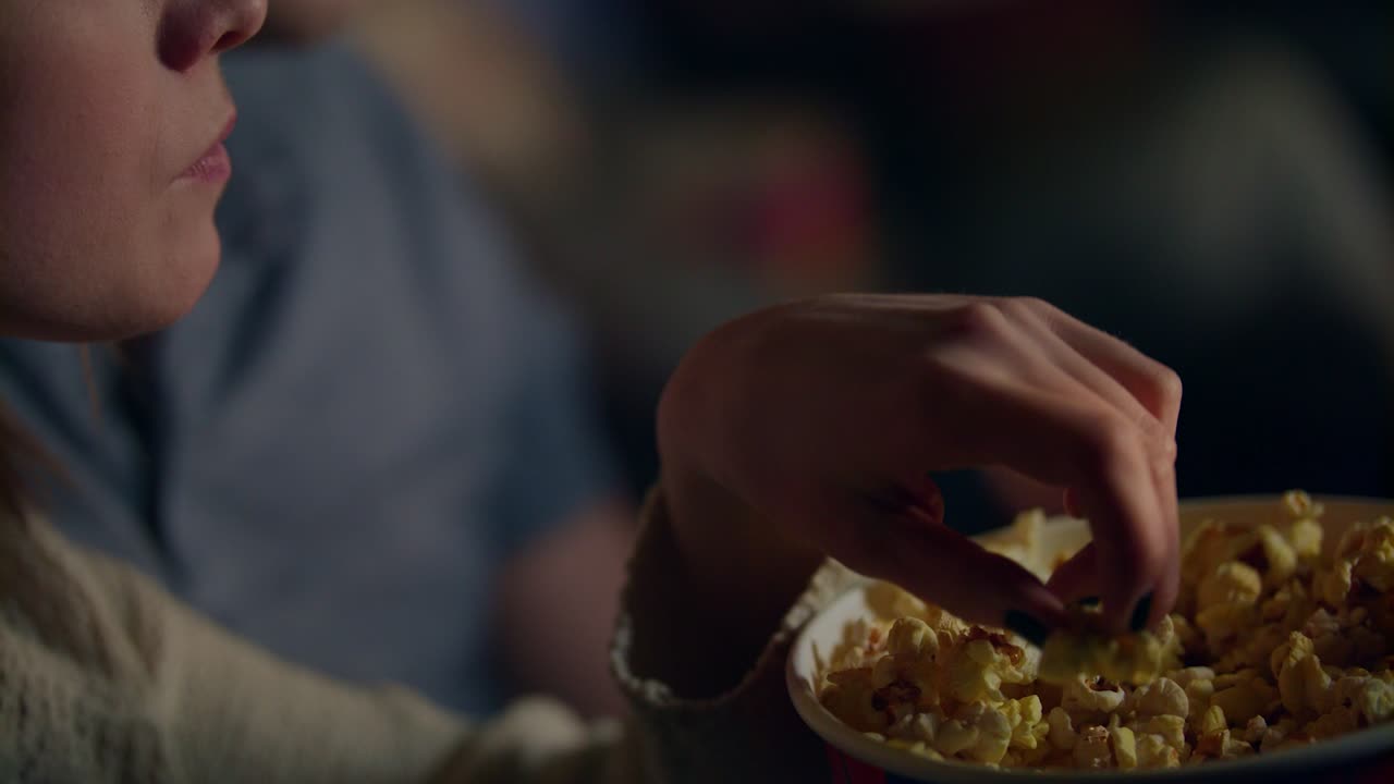 Ragazza che prende i popcorn da un secchiello di carta e li porta alla bocca. Una donna mangia popcorn al cinema.