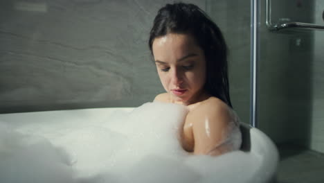 relaxed girl sitting in bath in loft interior. sweet woman resting tub indoors