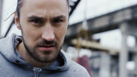 close-up view of young man with aggresive look posing in front of the camera with boxing moves outdoors an abandoned factory on a cloudy morning