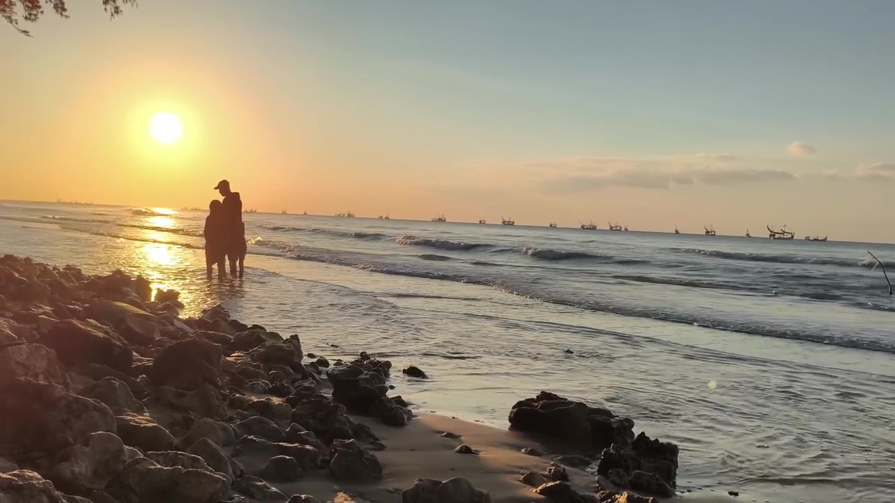 Silhueta de Família Caminhando na Praia ao Pôr do Sol Dourado com Barcos de Pesca