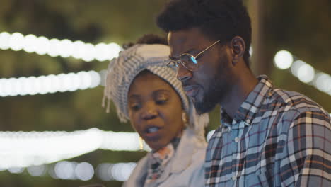 black man and woman discussing something on laptop in park in evening