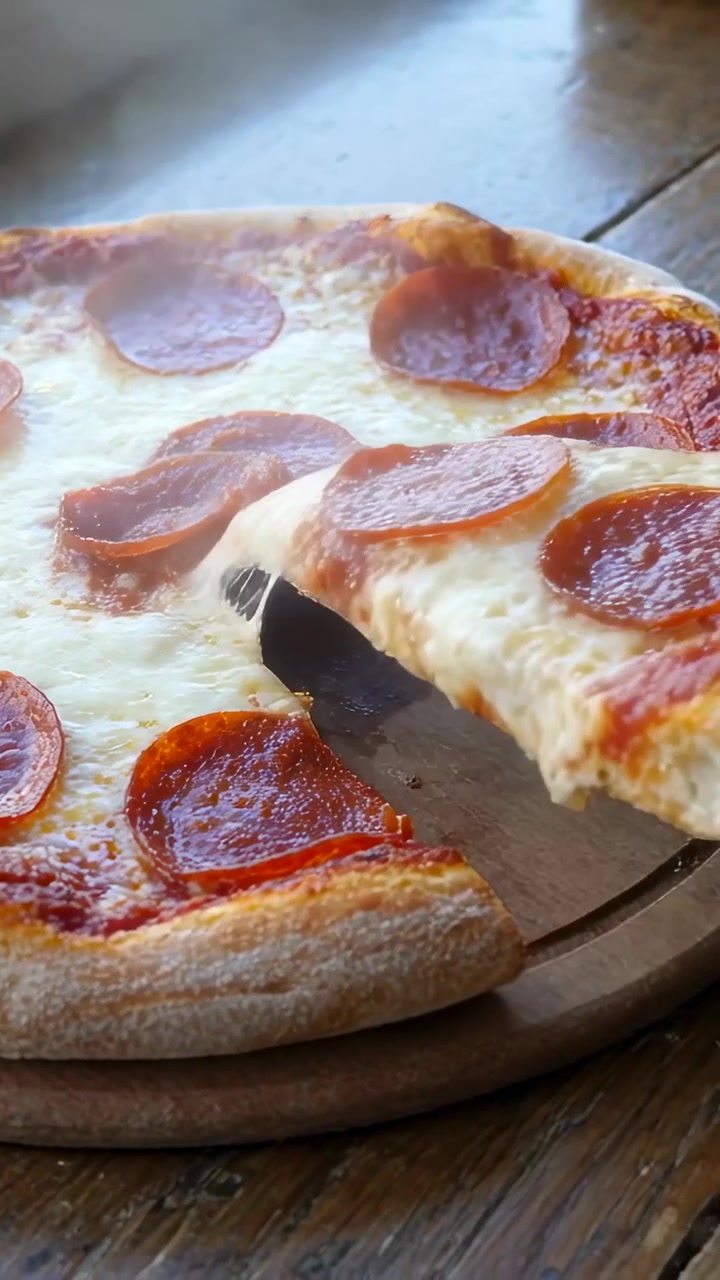 Video verticale: Spatola che scivola sotto una fetta, mano che solleva una fetta di pizza ai peperoni vicino alla finestra, servendo.