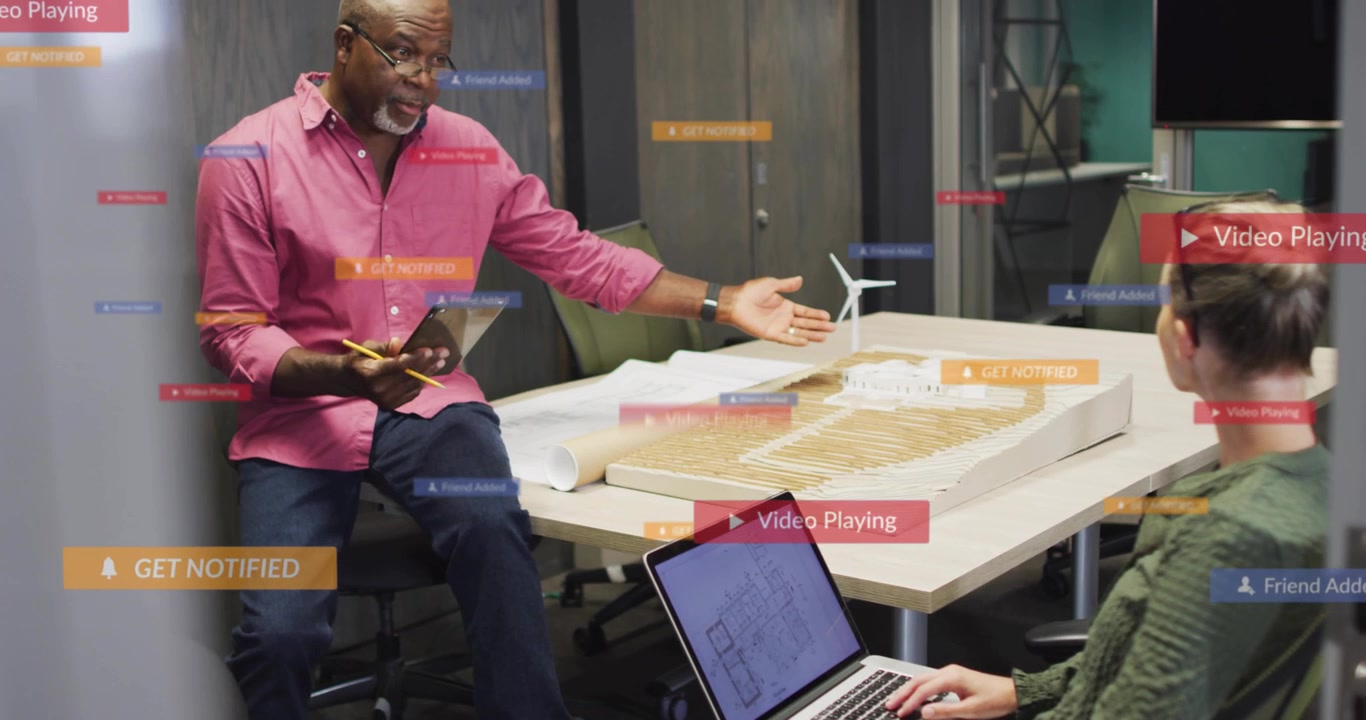 Vertical video: Man unrolling plan and placing turbine while peer typing, showing design with UI