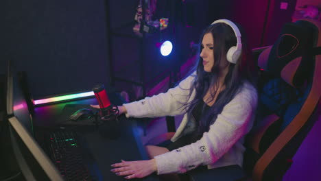 overhead view of frustrated girl in headset hitting desk in irritation while working on task in colorful studio setup and red condenser mic, expressing visible anger and dissatisfaction