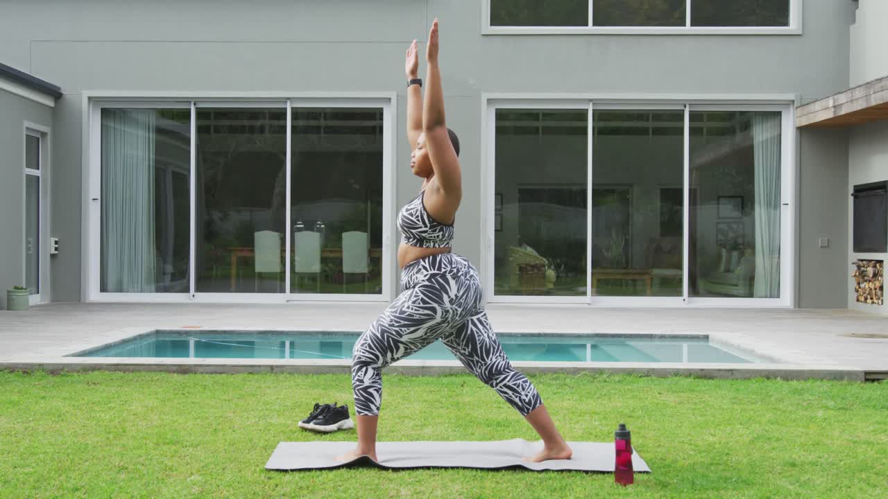 feliz mujer afroamericana de talla grande practicando yoga, de pie estirándose en el jardín